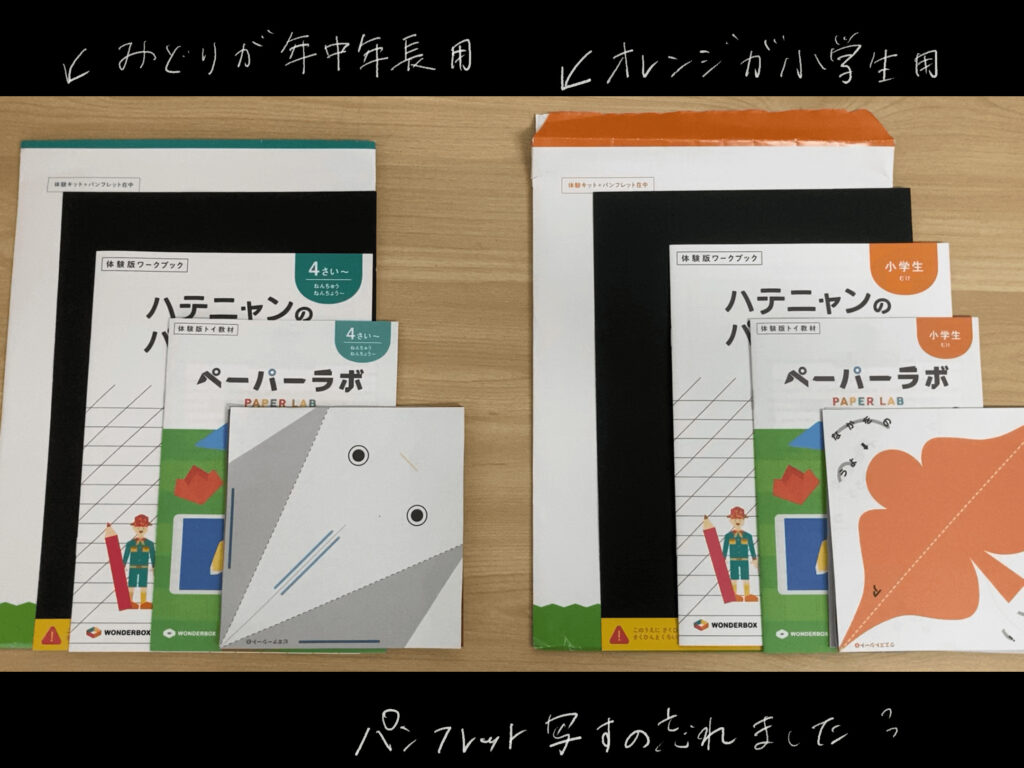 木製の机の上に、二人分のWANDERBOXの無料資料請求で届いた教材が並んでいる写真。左には年中年長用の緑色の開封済の封筒。年中年長用の黒い台紙。年中年長用の体験ワークブック、ハテニャンのパズルノート、年中年長用の体験版トイ教材、ペーパーラボ。目のイラストが描かれた、白と灰色２色の折り紙。　右には小学生向けのオレンジ色の開封済みの封筒。黒い台紙。小学生むけ体験版ワークブック、ハテニャンのパズルノート。小学生向け体験版トイ教材、ペーパーラボ。オレンジ色の鳥のようなイラストとひらがながかいてある折り紙が並んでいる。