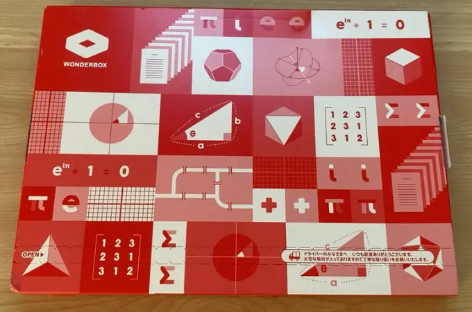 木製の机の上に赤い箱が乗っている写真。赤い箱には、WONDERBOXと書かれている。また赤い箱のデザインは数字や図形、記号など数学に関係したものである。