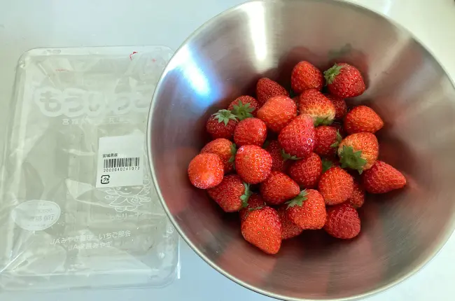 白いキッチントップ背景。苺の空パックが1つと、苺が入った柳宗理のステンレスボール19cmが並んでいる写真。